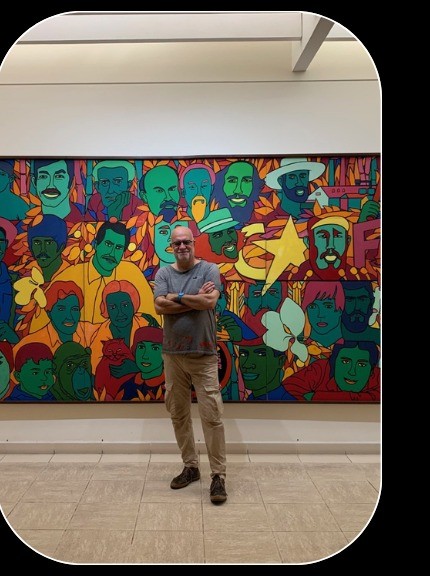 Andrea Schettin in piedi davanti a un grande murale colorato